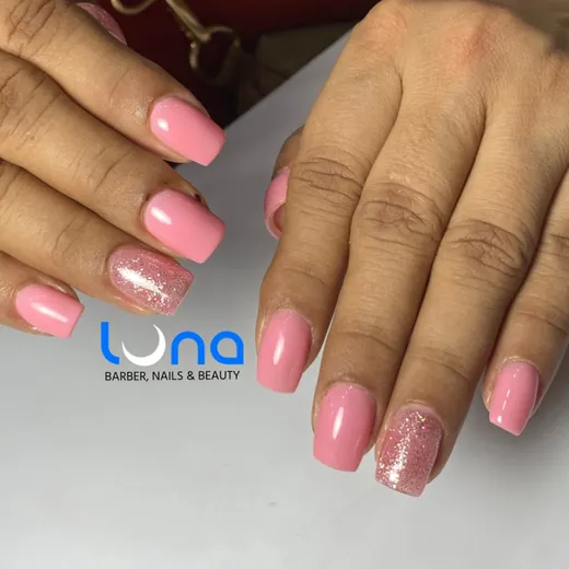 Uñas rosadas con una uña de brillo, sobre la mesa del salón